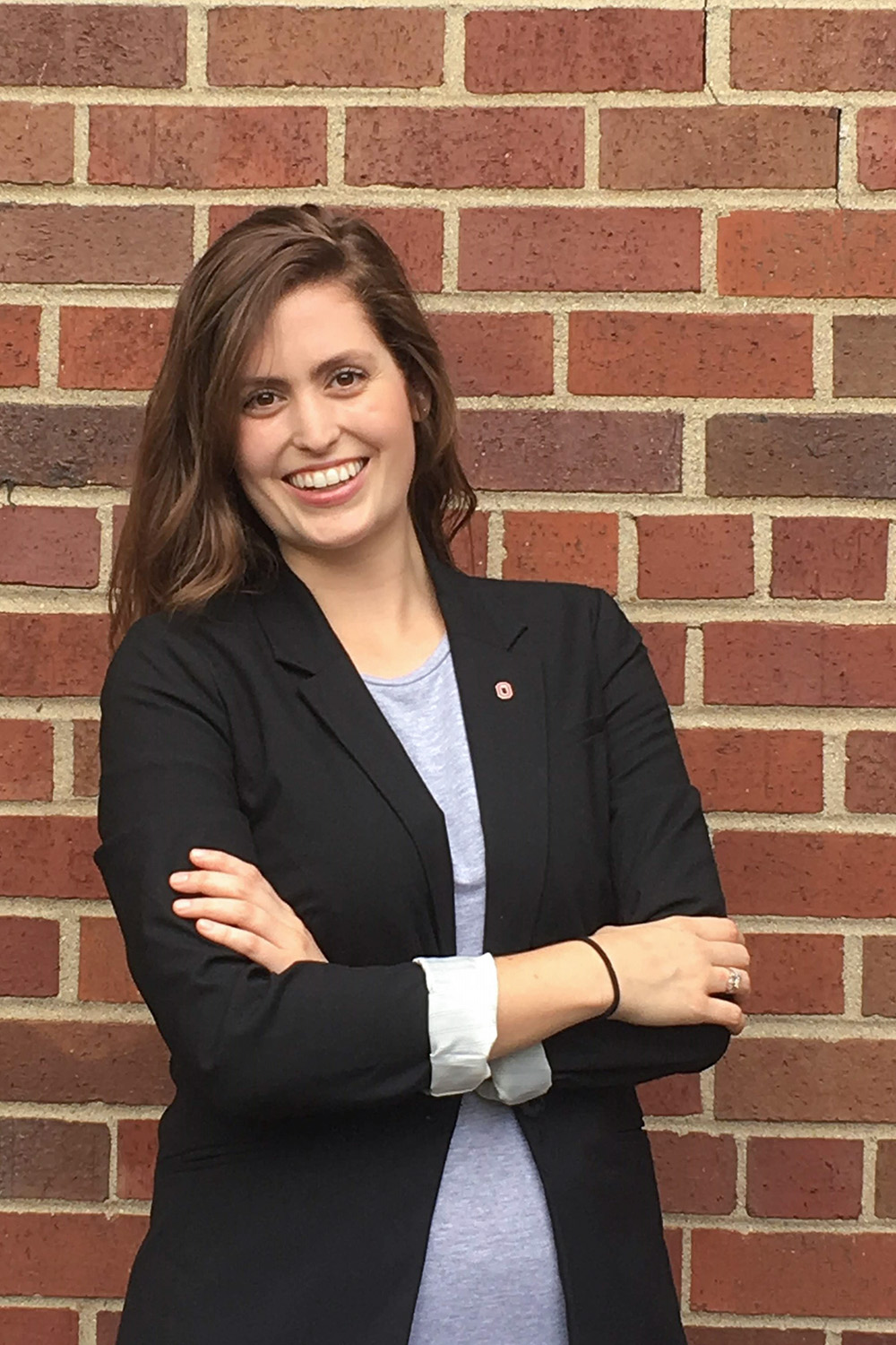 Portrait of Katie McAfee is black blazer and grey shirt on brick wall