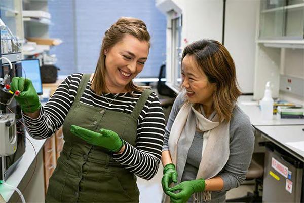 Two postdoc students smiling while in a lab working on their research