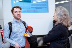 A graduate student holding a donut while gesturing and speaking with Dean Stromberger at the 2024 Donuts with the Deans Event.