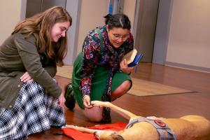 Two female graduate students petting the greyhound therapy dog at the Donuts with the appreciation week kick off events.