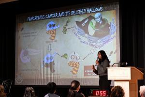 Ayushi Das presenting on a stage in front of a presentation