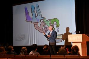 Jason A. Christman presenting on a  stage in front of a presentation