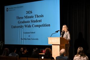 Mary Stromberger introducing the three minute thesis behind a podium on a stage