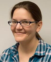 A photo of Lisa Barrow smiling wearing glasses and a blue-green and white plaid shirt.