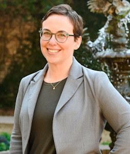 A photo of Marta Bornstein wearing a grey blazer, green blouse, and glasses.