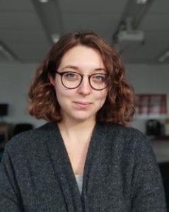A photo of Maria Copot smiling wearing a grey sweater and glasses.