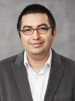 A picture of Eduardo Reategui smiling at the camera wearing glasses, white shirt, and grey blazer.