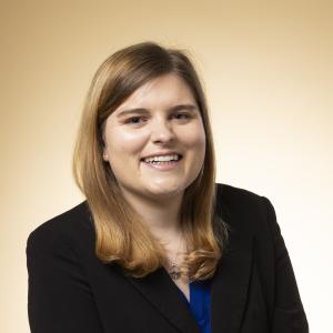 A photo of Mia Hoffman smiling wearing a black blazer and blue dress shirt.
