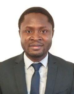 A photo of Muhedeen Lawal smiling wearing a grey blazer and blue tie.