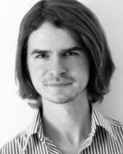 A black and white photo of Nikita Makarchev smiling wearing a pinstripe dress shirt.