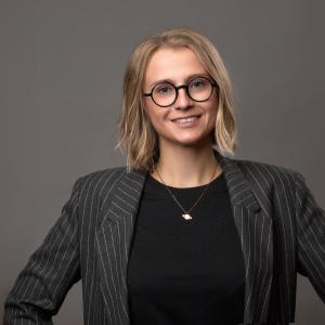 A photo of Maria Stefaniak smiling wearing a black blouse, grey blazer, and glasses.