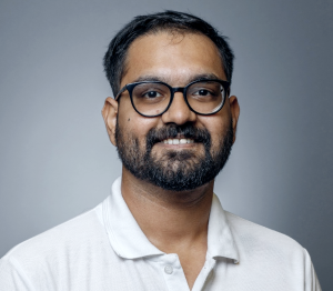 Photo of Abhishek Mishra smiling wearing a white polo shirt and glasses.