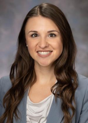 A photo of Emily Moscato smiling wearing a white blouse and blue blazer.