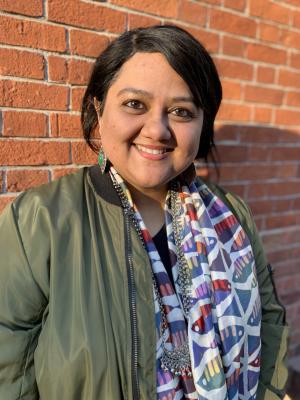 A picture of Manjari Mukherjee smiling wearing a green jacket with a brick wall in the background
