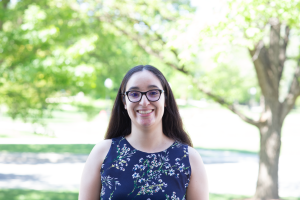 A picture of Camila Olivero Araya in a blue dress and glasses with trees in the background.