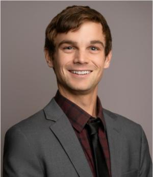 A photo of Justin Palmer wearing a grey blazer and maroon dress shirt.