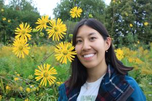 A photo of Michelle Pham smiling with flowers and green foiliage in the background.