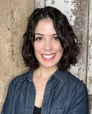 A photo of Taban Salem wearing a denim dress shirt and black blouse with wood paneling in the background.