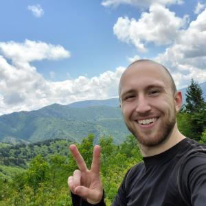 A photo of Eric Shershen smiling at the camera with a mountain landscape in the background.