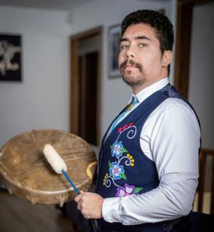 A photo of N. Deondre Smiles in a blue floral vest and blue dress shirt and tie holding a drum and mallet