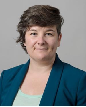 A photo of Sam Sommers smiling wearing a green blouse and blue-green blazer.