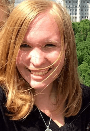 A photo of Erin Westgate smiling wearing a black shirt with green foliage in the background.