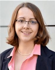 A photo of Kristin Wicke smiling wearing glasses, a pink dress shirt, and blue blazer.