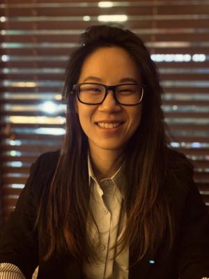 A photo of Lucy Lu smiling wearing a black cardigan, white button up shirt and glasses.