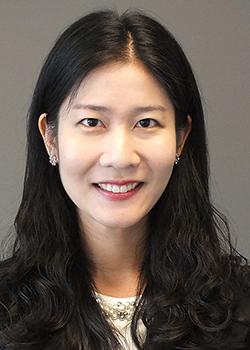 Susan Yoon Portrait with dark hair and a dark blazer on a grey background.