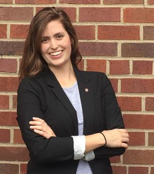 Portrait of Katie McAfee is black blazer and grey shirt on brick wall