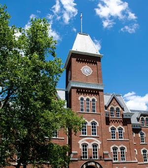  University Hall on the sunny day with sparse clouds with a green leafy tree in the foreground.